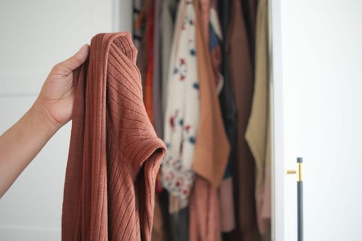 A person holds a textured brown piece of clothing while standing near a closet.