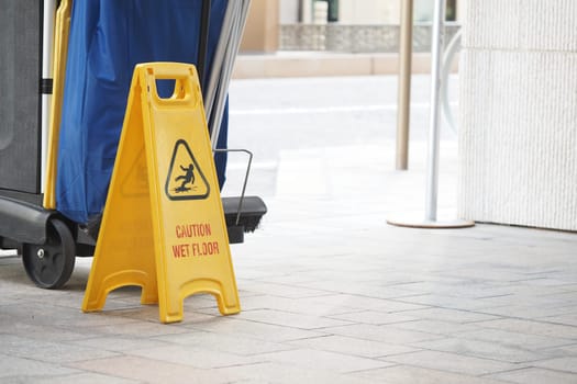 Bright yellow caution sign warns about a wet floor near cleaning tools.