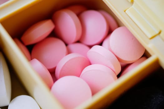 Close-up of pink tablets stored in a yellow pill organizer for easy access.