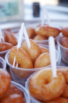 Mini donuts with a golden crust served in cups at a lively market.