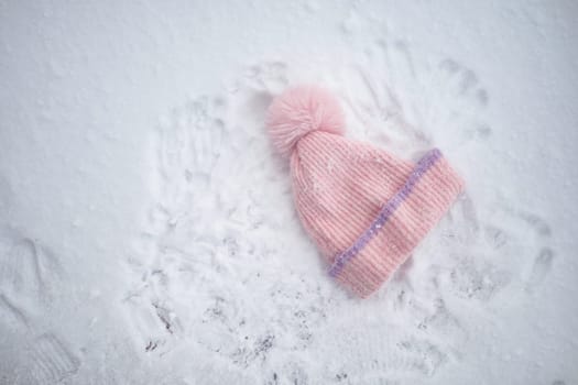 A soft pink hat lies in the snow surrounded by playful handprints.
