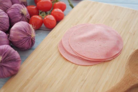 Fresh slices of deli meat are arranged on a wooden board with vegetables.