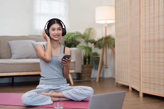 A happy woman sits cross-legged on a yoga mat, connecting with others through her phone while enjoying a peaceful moment.