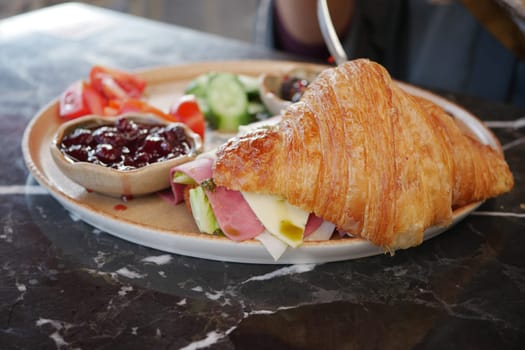 Fresh croissant sandwich with ham, cheese, and veggies.