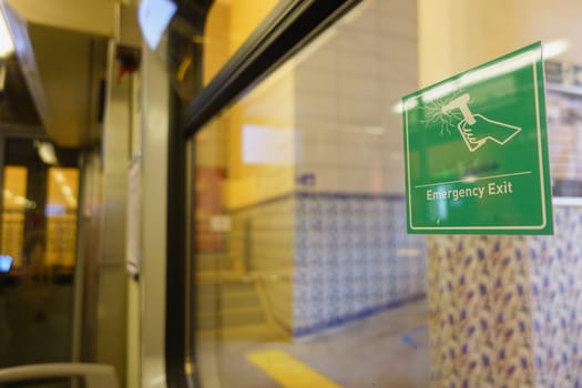 Sign indicating emergency exit located at busy transit station.
