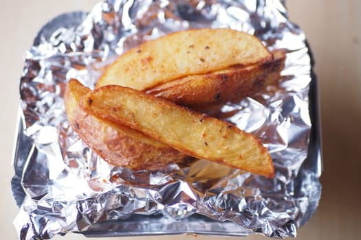 Golden brown potato wedges are arranged on foil in a tray, ready to enjoy.