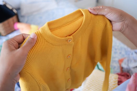 Hands grasp a yellow cardigan amid a colorful assortment of clothing.