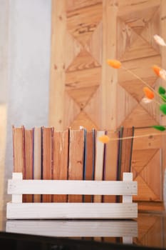 Wooden holder filled with colorful books placed on a table beside flowers.