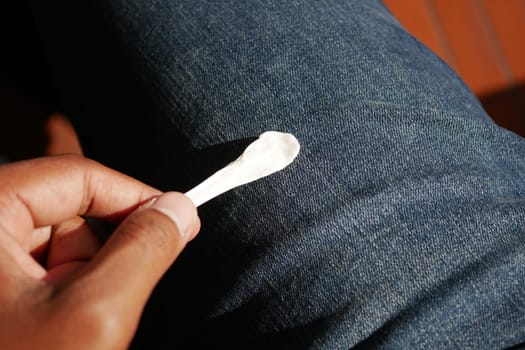 Hand holds a piece of chewing gum resting on blue denim jeans.