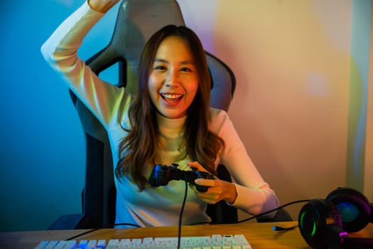 Winning. Happy Gamer using joystick controller for virtual tournament plays online video game with computer she raises hands to wins celebrating, Asian woman wearing gaming headphones feeling excited