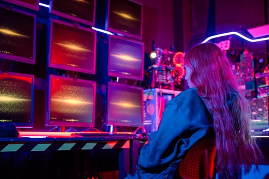 Asian woman holding laptop computer with CCTV room she check maintain security in monitor display, Hacker wearing a black jacket and has long red hair with multiple computer monitors