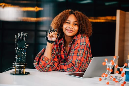 In a classroom a Black teenage student tests a robotic arm delving into subjects of interest. Embracing innovation and technology for skill development and joyful learning.