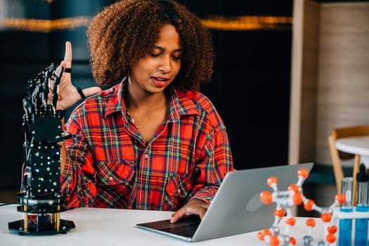 Portrait of a Black teenage student in a classroom learning about a robotic arm for her engineering project. She skillfully controls the arm showcasing intelligence and innovation in technology.