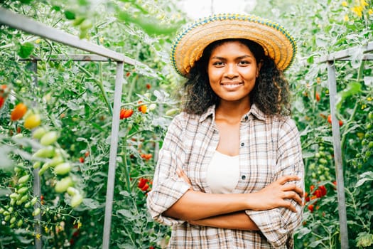 A cheerful woman farmer arms crossed tends to vegetables in a tomato greenhouse. Her smiling portrait reveals dedication and happiness in nurturing growth outdoors.