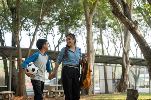 A nurturing mother and her son walk hand-in-hand through a park after school, blending education with outdoor play and quality time together.