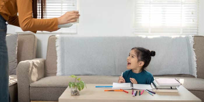 A mother surprises her excited daughter with a healthy snack while she is engaged in her artistic activities, emphasizing nourishment and joy.