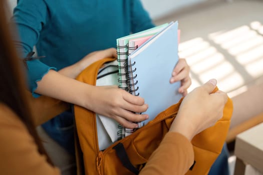 A mother assists her daughter in packing essential school supplies into a bright orange backpack, highlighting the importance of organization and preparation for school.