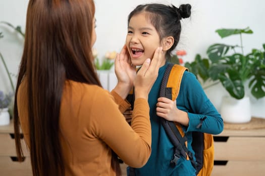 In a warm home environment, a mother playfully engages with her daughter, putting on her backpack and sharing smiles before she leaves for school, emphasizing their strong bond.