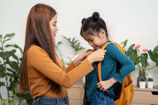 A dedicated mother helps her daughter put on her backpack, ensuring she is ready and prepared for the school day ahead, embodying the spirit of care and support.