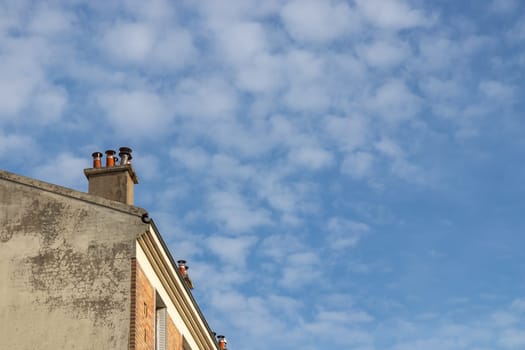Old brick chimney pipe without a smoke on the building's roof. Blue cloudy sky above the roof is a copy space. Repairing, reconstruction of house with own stove heating