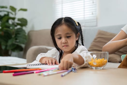 A young girl sets up her study space with vibrant colored pens and a bowl of snacks, showcasing a fun yet focused approach to her learning routine at home.