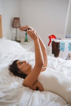 A woman comfortably lying on her bed, fully absorbed in her smartphone, radiating a relaxed modern lifestyle