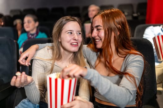Two female friends enjoying a movie night, sharing popcorn and laughs, creating a joyful and memorable cinema experience
