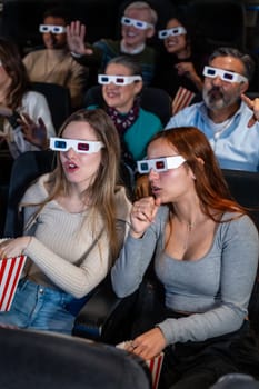 Group of diverse friends wearing 3d glasses enjoying a movie at the cinema, eating popcorn and experiencing reactions