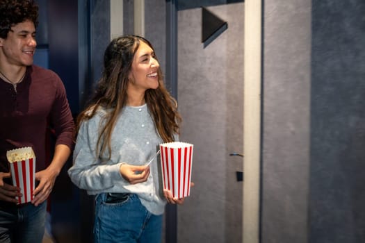 Happy couple walking into a movie theater, holding popcorn buckets and tickets, excited for the show