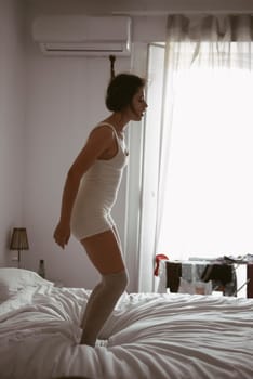 A woman energetically jumps on a bed, displaying her joy and carefree spirit in a tranquil indoor environment