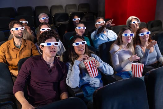 People of diverse ages wearing 3d glasses, eating popcorn, and watching a movie in a cinema, experiencing entertainment together