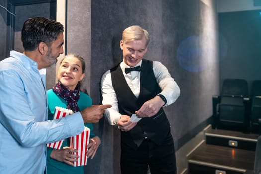 Couple holding popcorn buckets showing their tickets to the usher before entering the movie theater