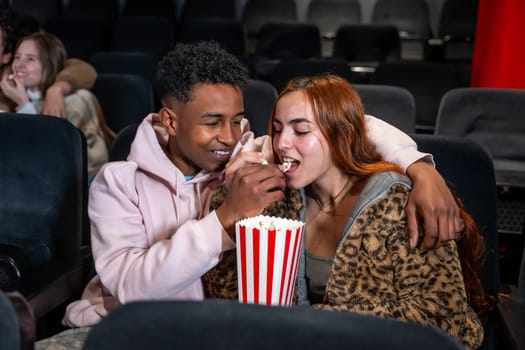Young couple enjoys a movie date, sharing popcorn and a tender moment in the darkened theater