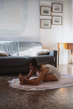 A young woman is practicing her yoga routine as she stretches on a mat in a bright, serene living space