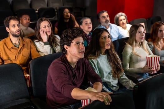 Captivated audience members of various ages and ethnicities experience a thrilling movie screening in a dark cinema, sharing moments of suspense and excitement