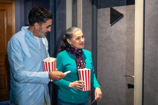Happy mature couple entering cinema theater with popcorn and tickets, enjoying a night out together