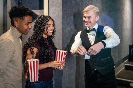 Young couple holding popcorn buckets entering a movie theater and checking their tickets with the usher before watching a film