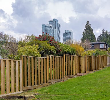 Wooden fenc in residential area with high-rise buildings on cloudy sky background.
