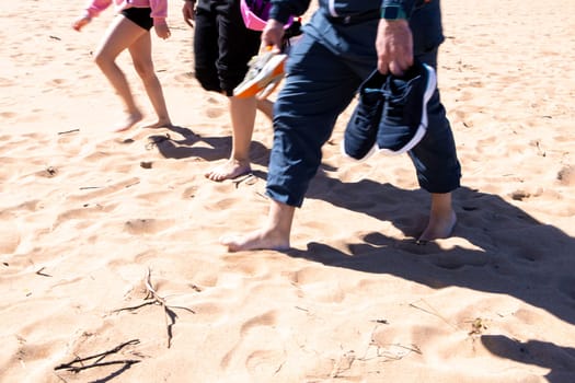 Group walking barefoot on sandy beach holding shoes.