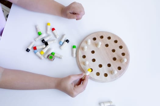 Child playing educational board game with wooden pegs and colored caps.