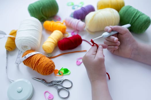 Child crocheting with colorful yarn and tools on white surface.
