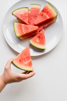 Child hand holding watermelon slice on white plate.