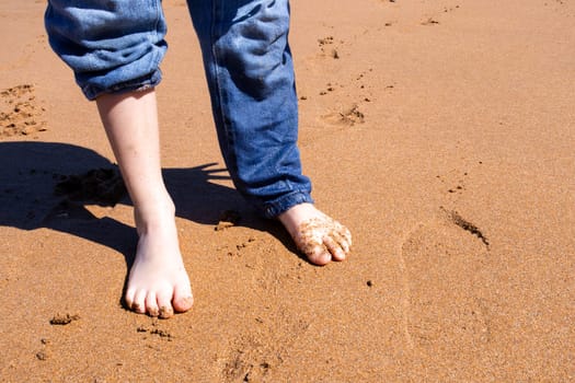 Child feet on sandy beach with rolled up jeans on a sunny day.