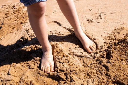 Toddler bare feet in the sand at a sunlit beach.