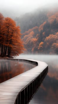 A curved wooden pathway over a misty lake, framed by vibrant autumn trees and foggy hills.