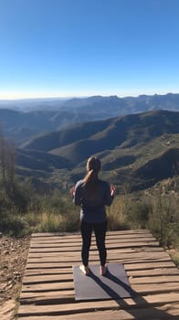 A woman meditating on a mountain deck with a breathtaking view of rolling hills and clear blue skies.