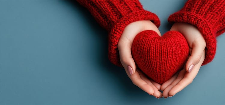 Warm hands in red knitted sweaters gently hold a red knitted heart, symbolizing love and care.