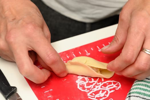 A person meticulously shapes a dumpling wrapper, carefully folding the edges to seal in a delicious filling, while a soft glow fills the inviting kitchen on a rainy day.