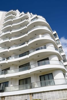 A striking building features flowing balconies and a sleek facade against a clear blue sky, highlighting contemporary architectural beauty on a sunny day.