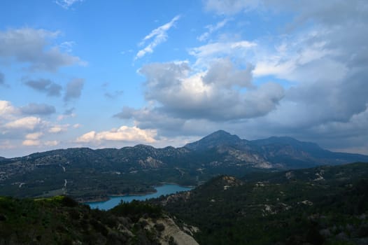Breathtaking hills tower over a tranquil lake, framed by fluffy clouds and a brilliant sky. Nature's beauty captivates during the late afternoon light, inviting exploration and tranquility.